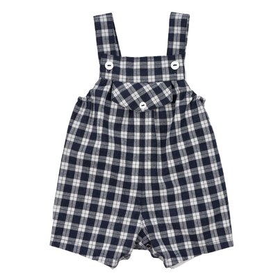 Jardineiras de perna curta para bebé em vaiela muito macia e ligeiramente cardada, quase uma flanela, ao xadrez azul e branco cru, com forro interior em tecido branco. Bolso no peito. Alças apertam à frente com botões brancos. Elásticos dos lados e molas no entrepernas. Vista de frente, fundo branco.