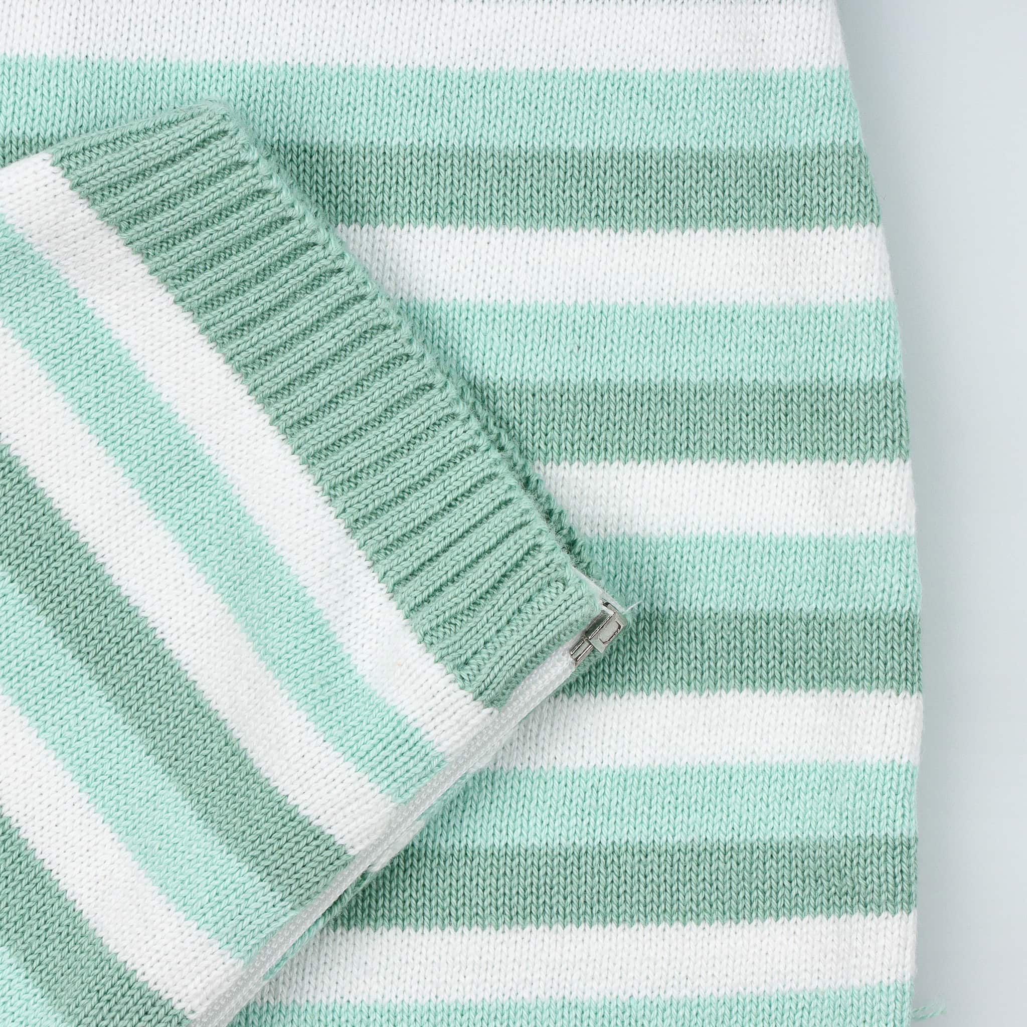 Detalhe de manga do fatinho de bebé tricotado às riscas brancas e diferentes tons de verde.