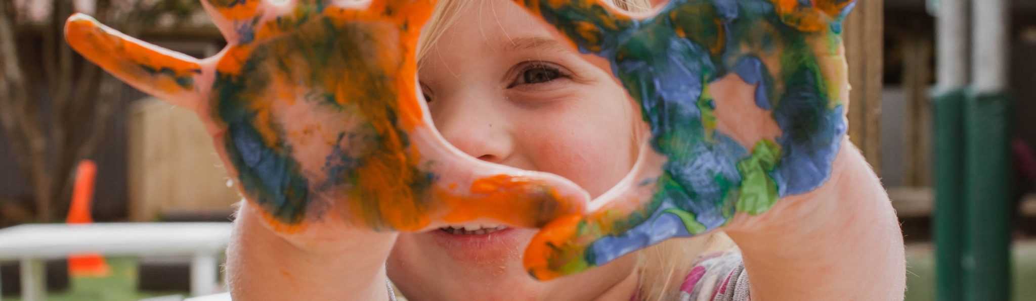 Cara de bebé com as mãos pintadas com tinta de várias cores.