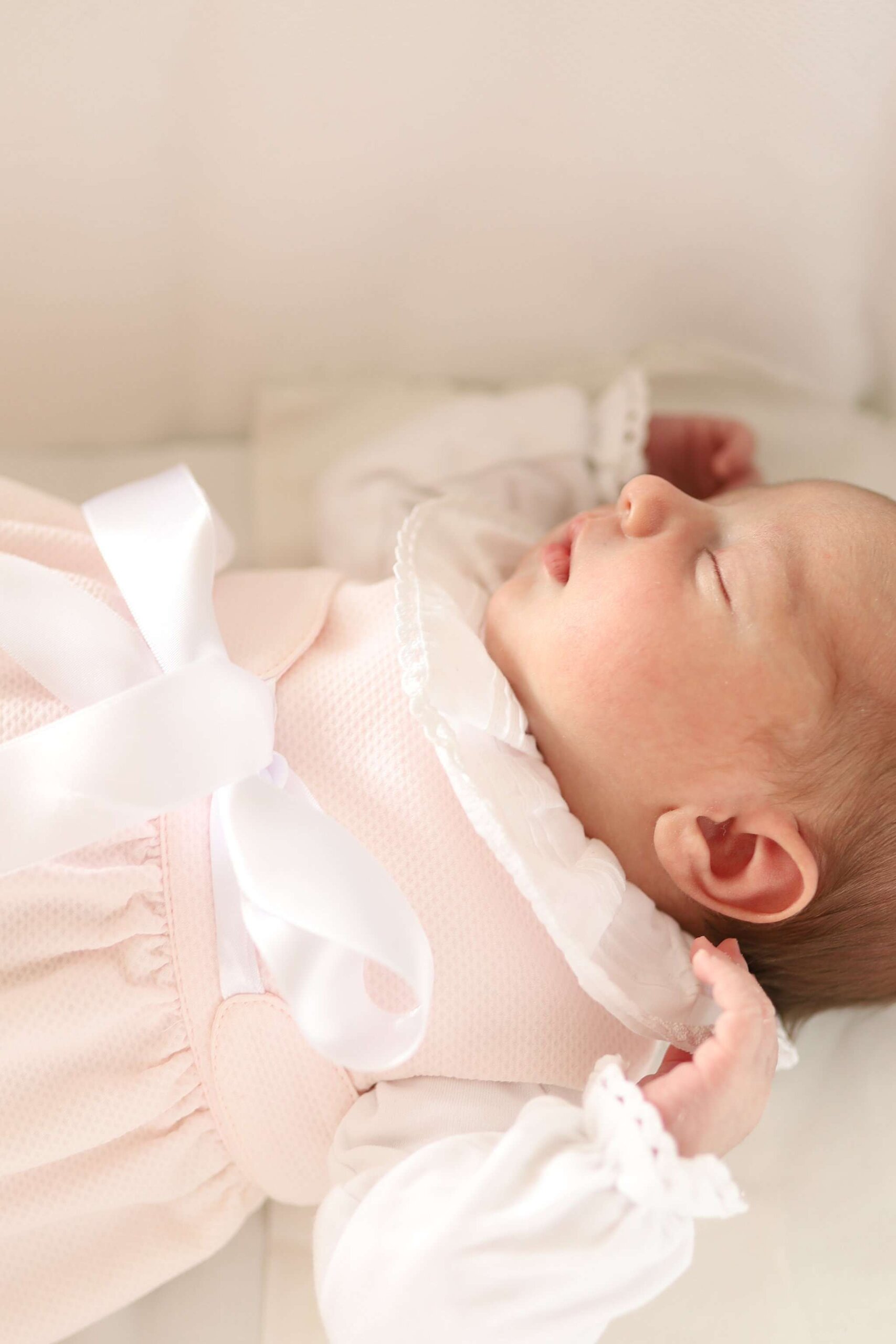 Bebé deitado a dormir vestido com um cueiro rosa e um body branco com gola.