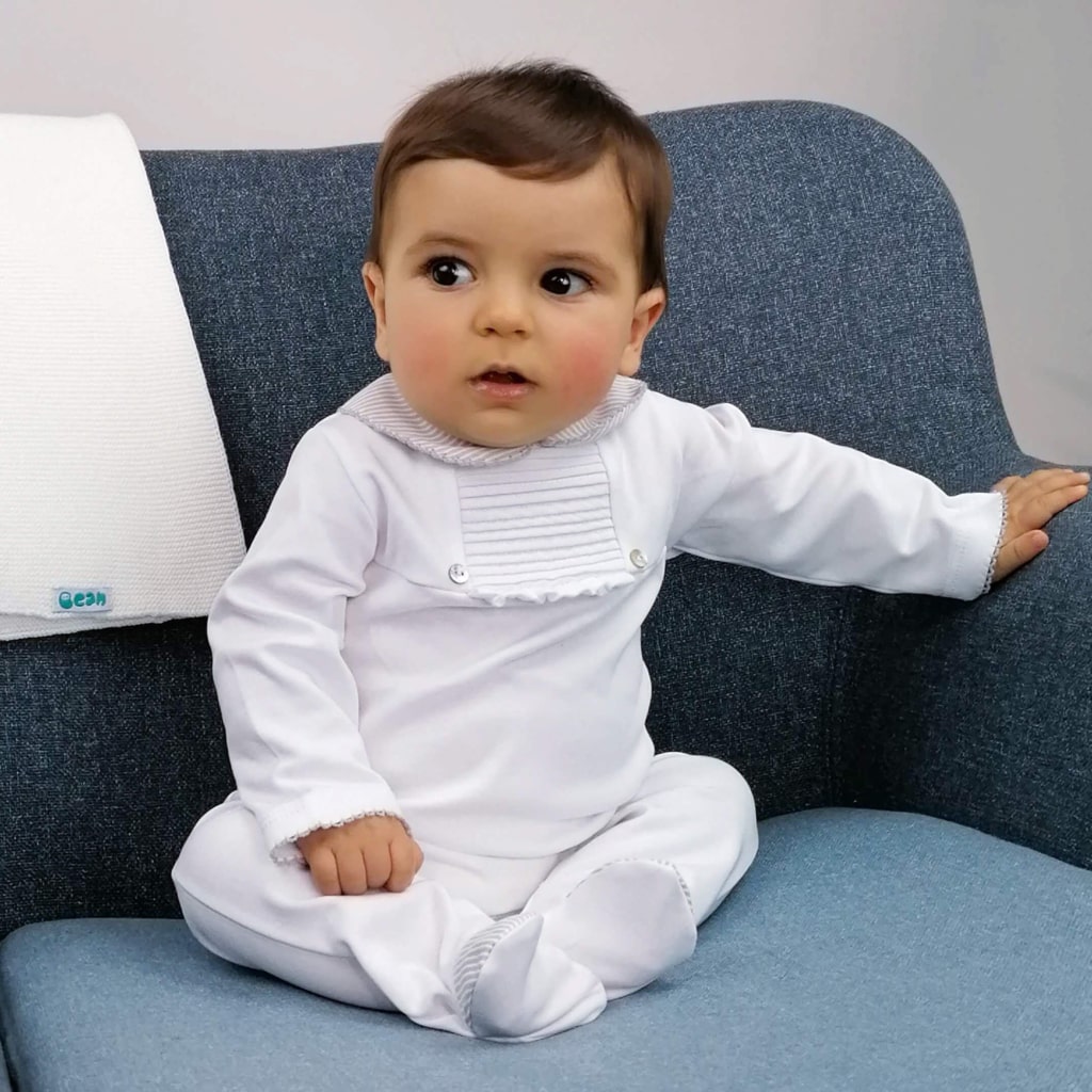Bebé sentado num sofá com um babygrow branco.