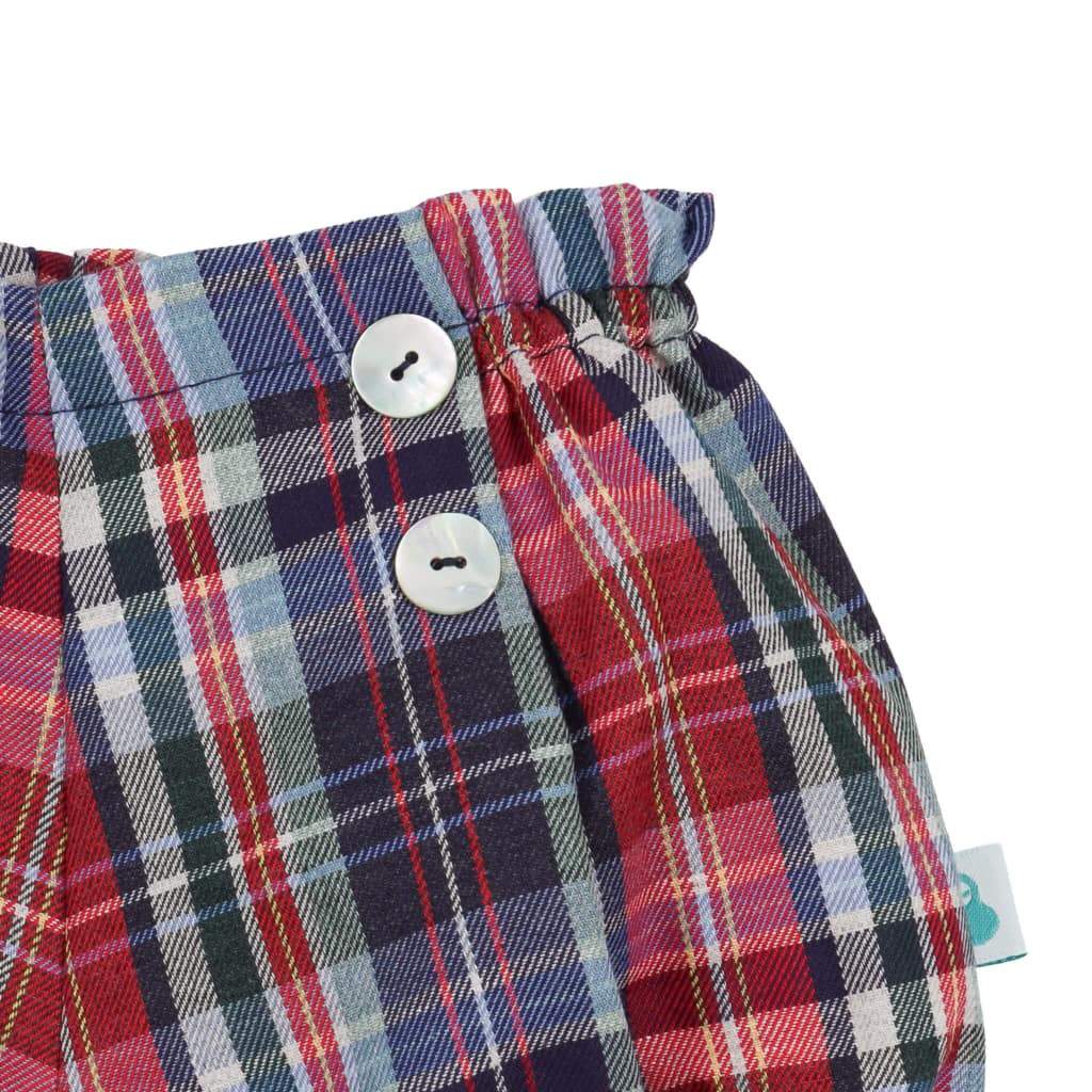 Pormenor dos botões de madrepérola de uns calções para bebé do tipo tapa fraldas feitos em tecido de xadrez com tons de azul e vermelho.