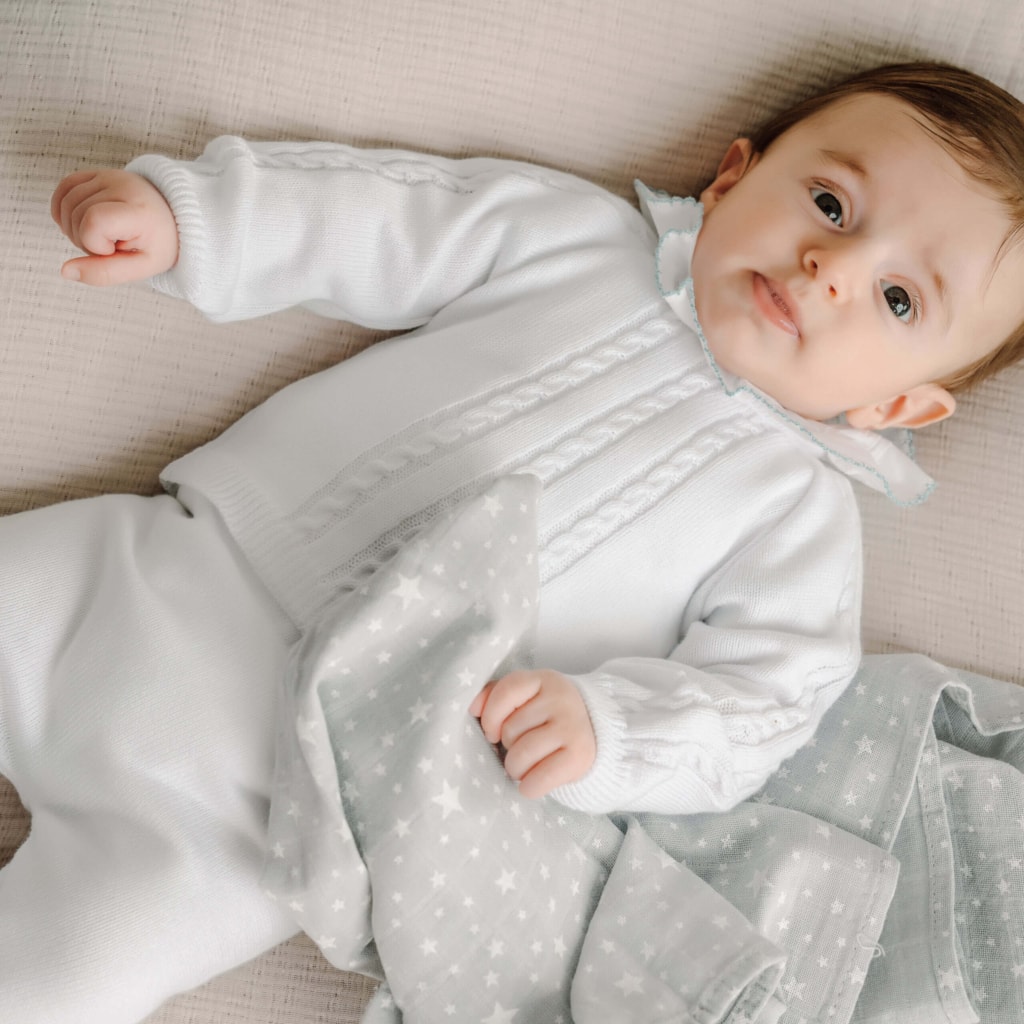 Bebé vestido com um conjunto de camisola de calças de malha brancos.