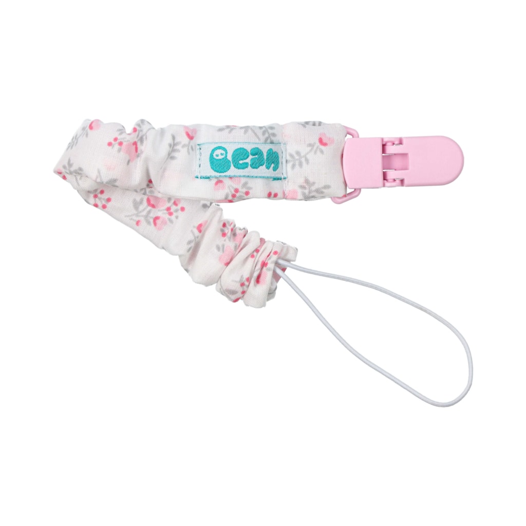 Porta chupetas para bebé dobrado feito em tecido de algodão branco com um padrão de flores rosa. Tem um elástico interior, fecho rosa em plástico e um elástico branco na ponta para prender a chupeta.