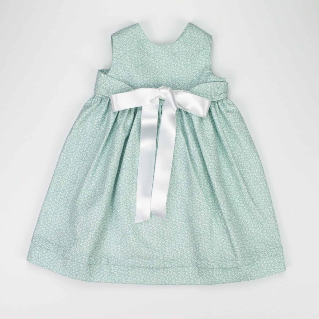 Cueiro para bebé em tecido verde com padrão de flores brancas e uma fita de cetim branca que fecha à frente em laço.