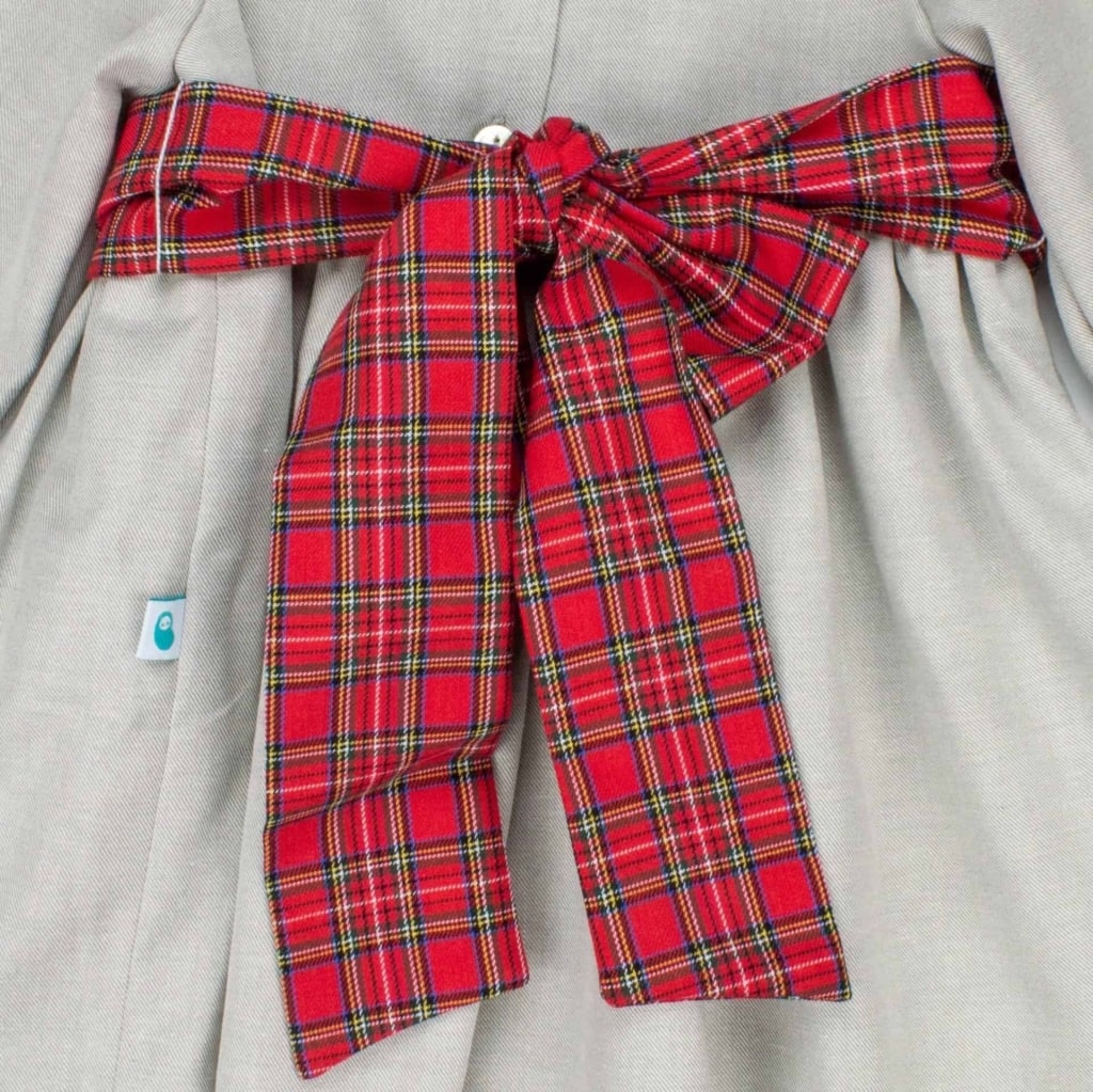 Faixa de tecido xadrez vermelho à cintura de um vestido de bebé em tecido cinzento.