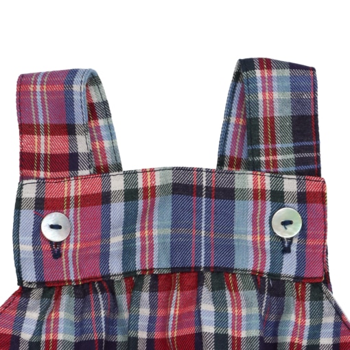 Pormenor das alças e dos botões de madrepérola de um fofo para bebé feito em tecido de xadrez com tons de azul e vermelho.