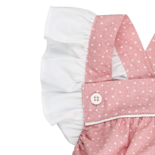 Folho branco nas alças de um fofo de bebé em tecido de algodão rosa claro com um padrão de estrelas brancas estampado. Tem botões de massa branca nas alças.