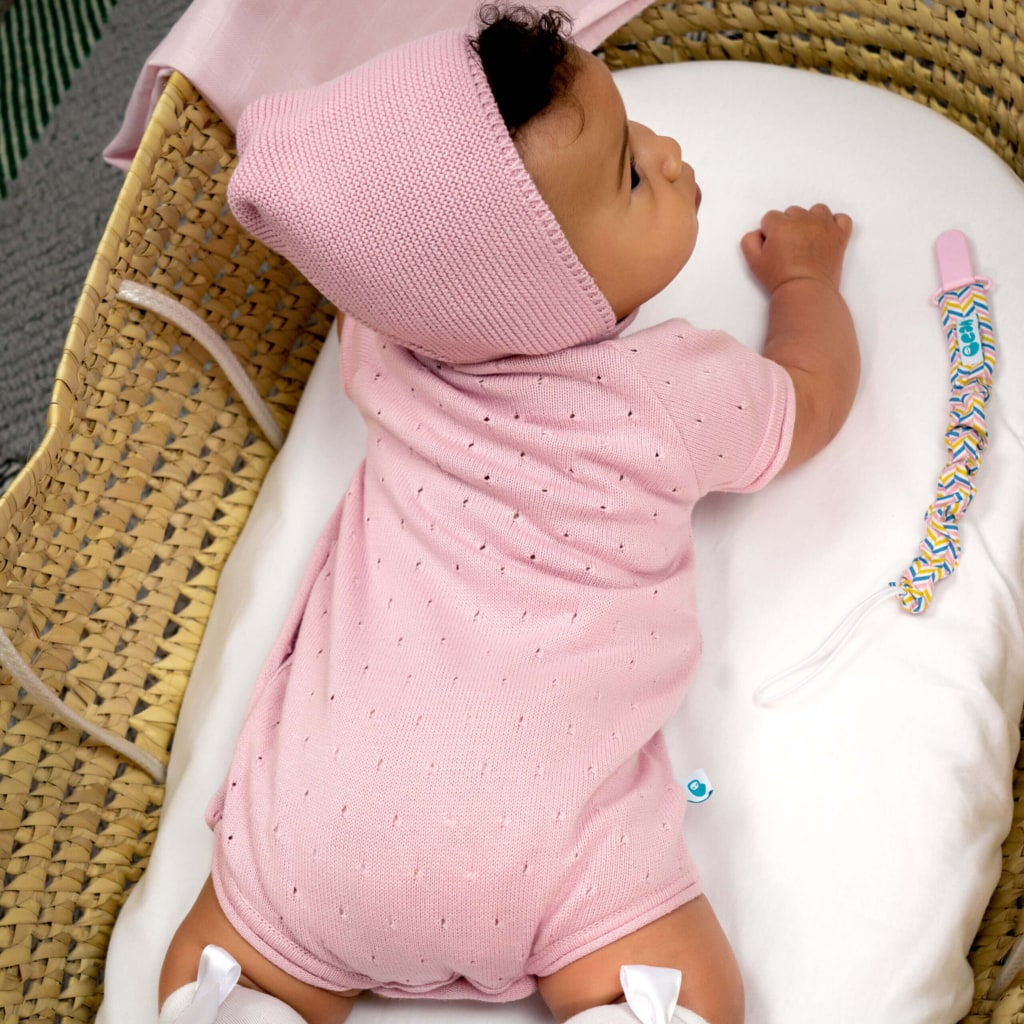 Bebé deitado de costas em alcofa vestido com um fofo cor de rosa de malha e uma touca de malha cor de rosa.