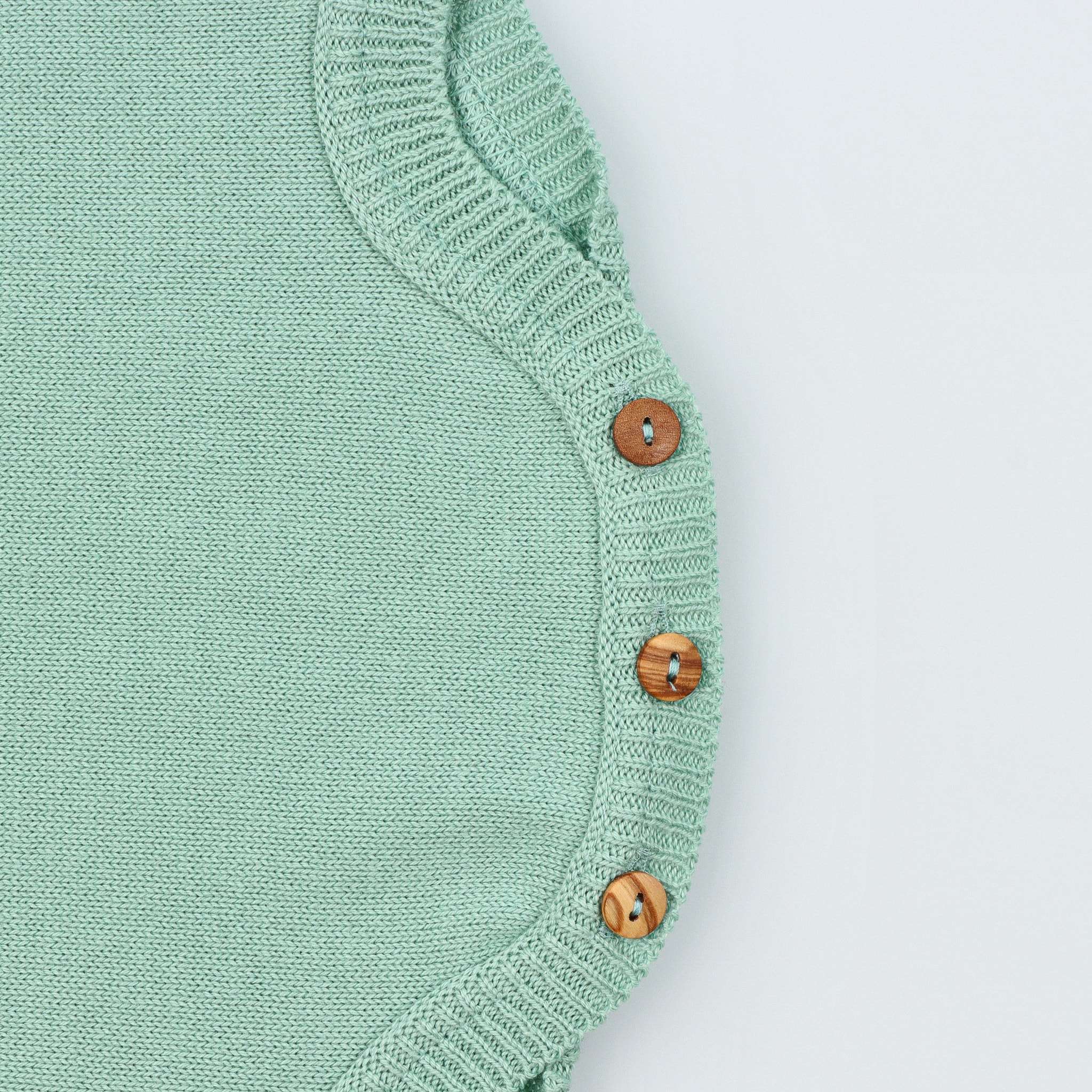 Detalhe de entrepernas, com botões de madeira fechados, do fofo de bebé em malha tricotada 100% algodão verde seco.