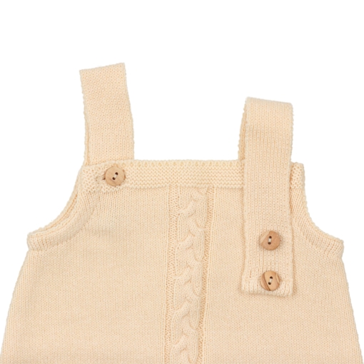 Pormenor das alças desabotoadas e dos botões em madeira de um fofo para bebé feito em malha amarela.