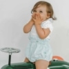 Bebé vestida com fofo de alças e body sentada em um carrinho.
