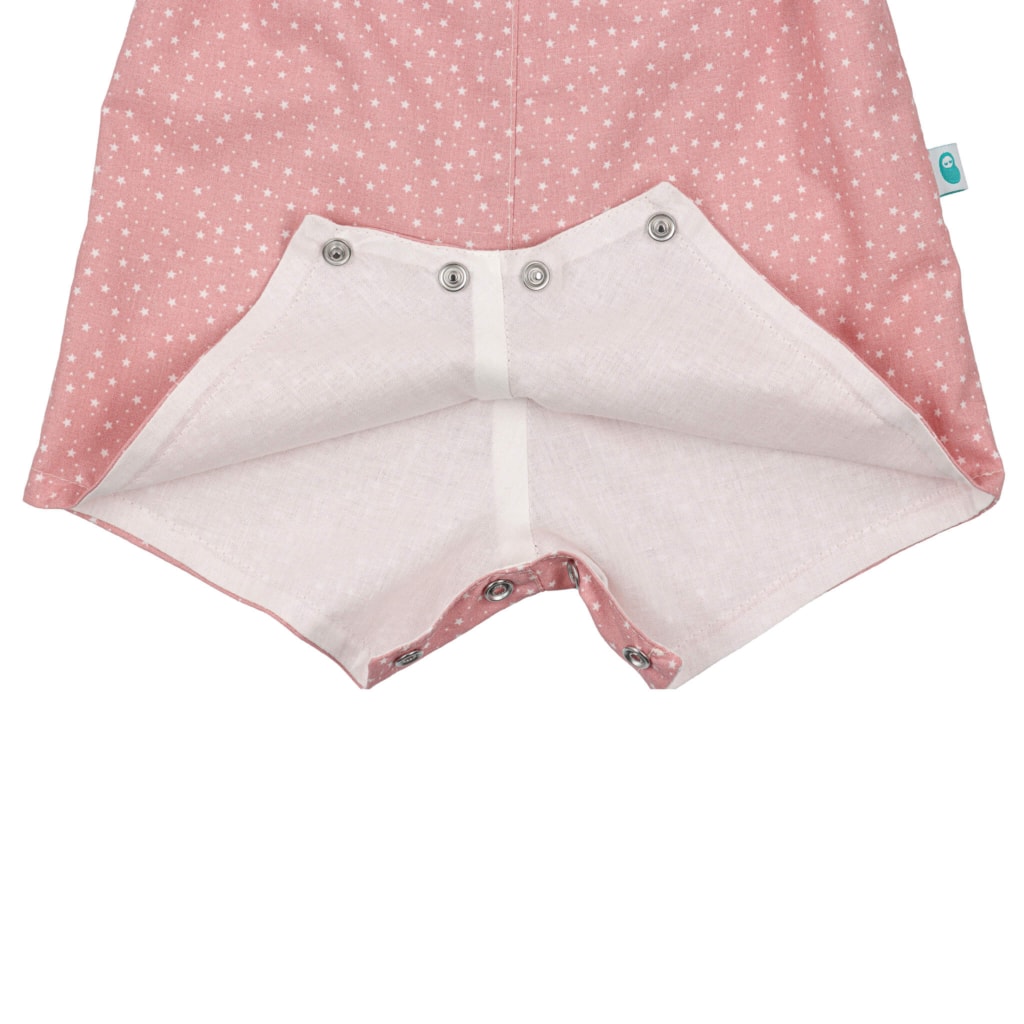 Vista do entre-pernas com três molas de pressão e do forro interior branco de umas jardineiras de bebé rosa com estampado em estrelas brancas.