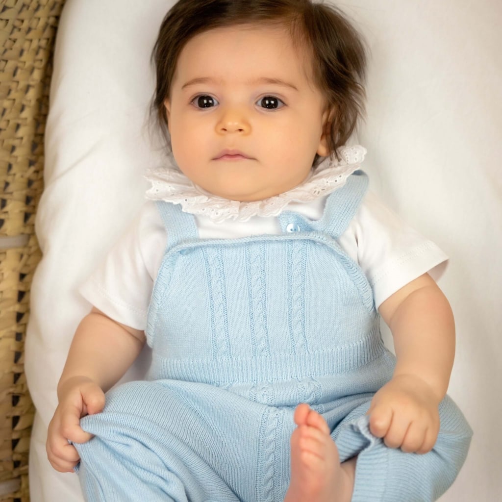 Bebé vestido com um body de gola e umas jardineiras de malha azul.