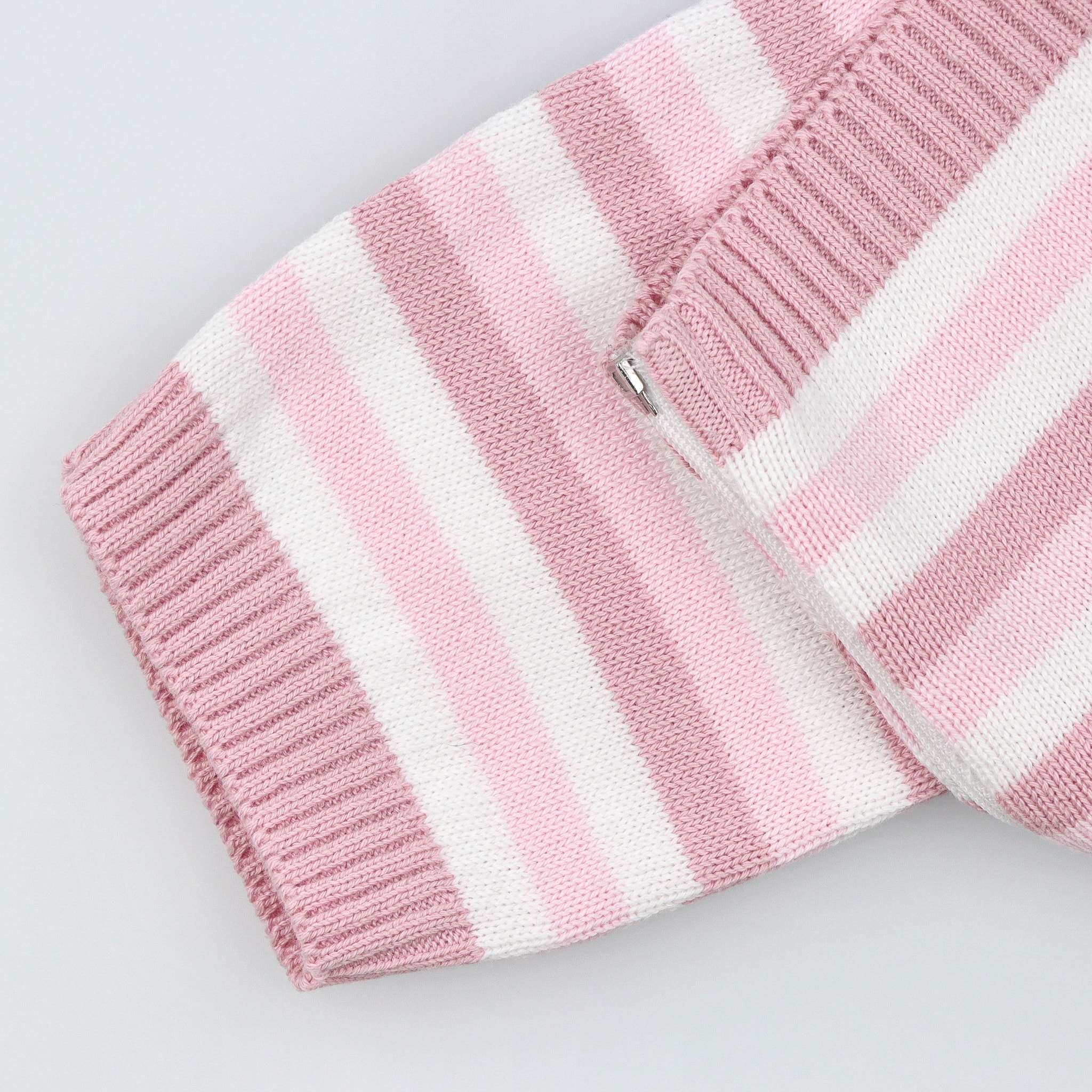 Detalhe de manga do fatinho de bebé tricotado às riscas brancas e diferentes tons de rosa.