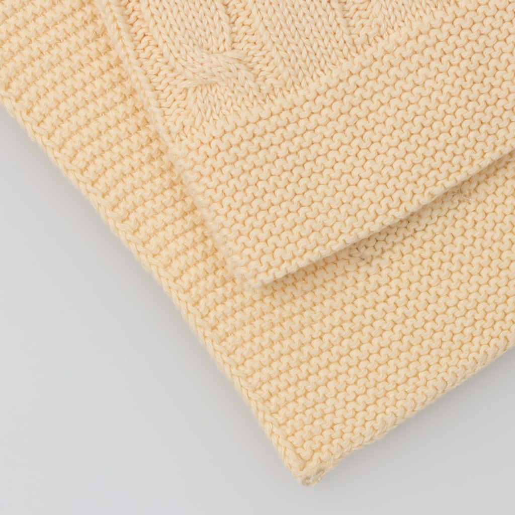 Pormenor do tecido em mala de algodão de uma manta para bebé amarela com padrão de tranças.