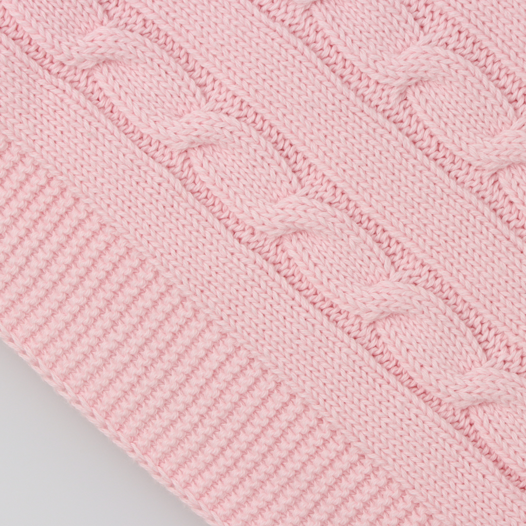 Pormenor do tecido em mala de algodão de uma manta para bebé rosa com padrão de tranças.