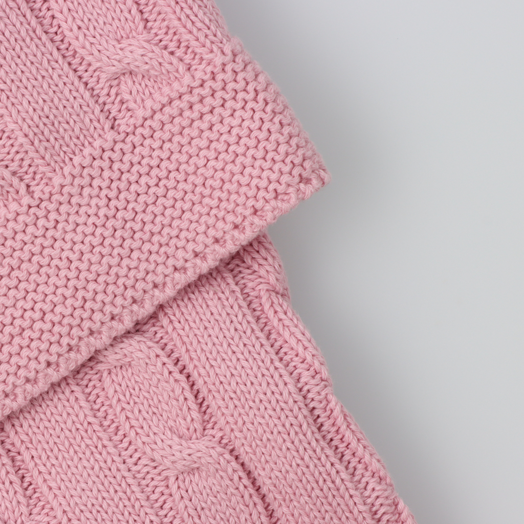 Pormenor do tecido em mala de algodão de uma manta para bebé rosa velho com padrão de tranças.