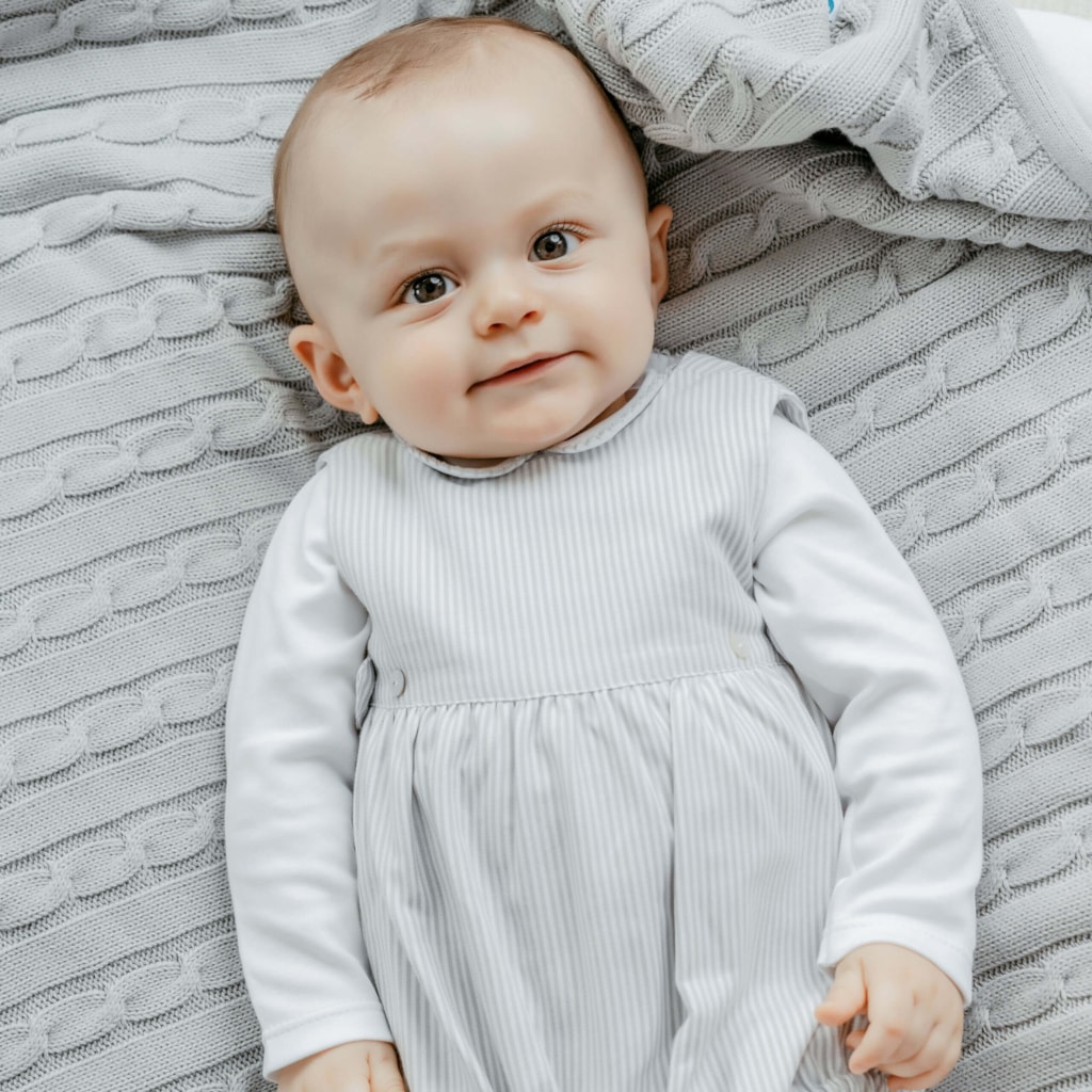 Bebé deitado sobre uma manta cinzenta de algodão.