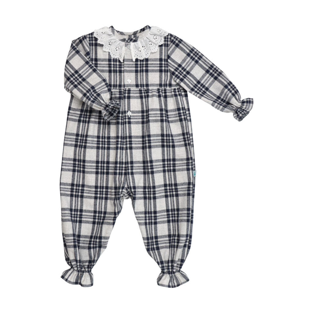 Pijama macacão para bebé menina feito em tecido xadrez de tons azul marinho e branco. Tem uma gola de renda branca e elástico nos punhos e tornozelos.