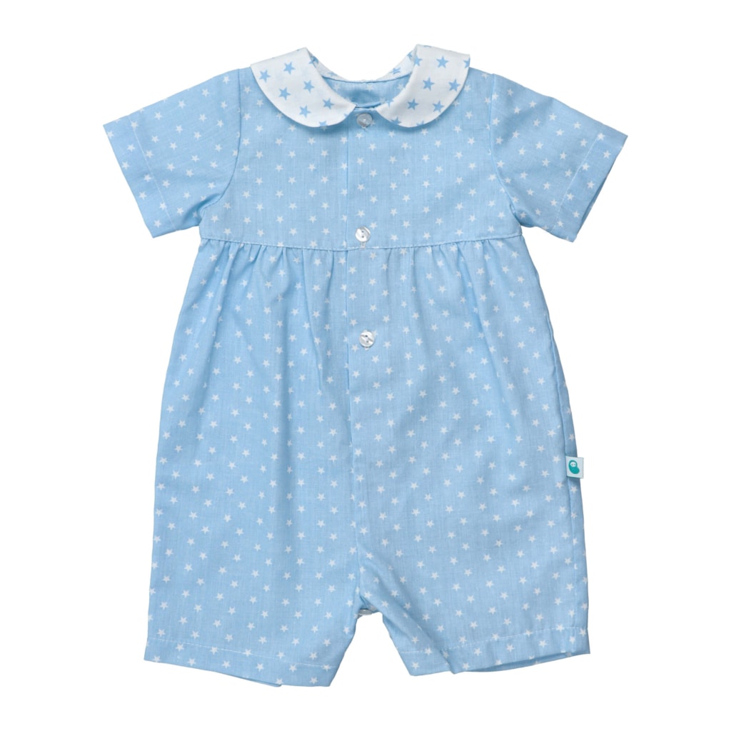 Pijama de bebé com perna curta feito em tecido azul de algodão com estampado de estrelas brancas. Tem manga curta, uma gola branca com estrelas azuis e fecha à frente com botões.