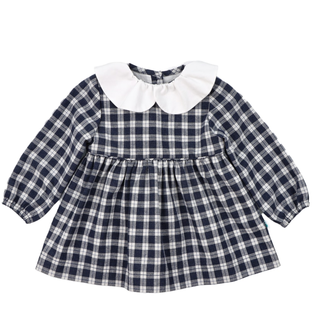 Vestido em tecido vaiela muito macia e ligeiramente cardada, ao xadrez azul e branco cru, com gola bebé em tecido branco. Aperta com três botões de massa brancos nas costas. Forro interior de algodão e elásticos nos punhos.